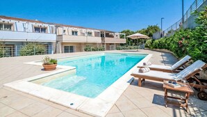 A swimming pool with lounge chairs and a small table, surrounded by a building with a tiled roof and a garden area. - Beautiful apartment for 4 people with WIFI, pool, A/C, TV, balcony and pets allowed (Viddalba)