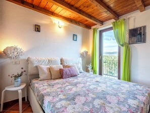 Ein Schlafzimmer mit Holzbalkendecke, einer blumigen Bettdecke und Blick auf die Landschaft durch eine Schiebetür.