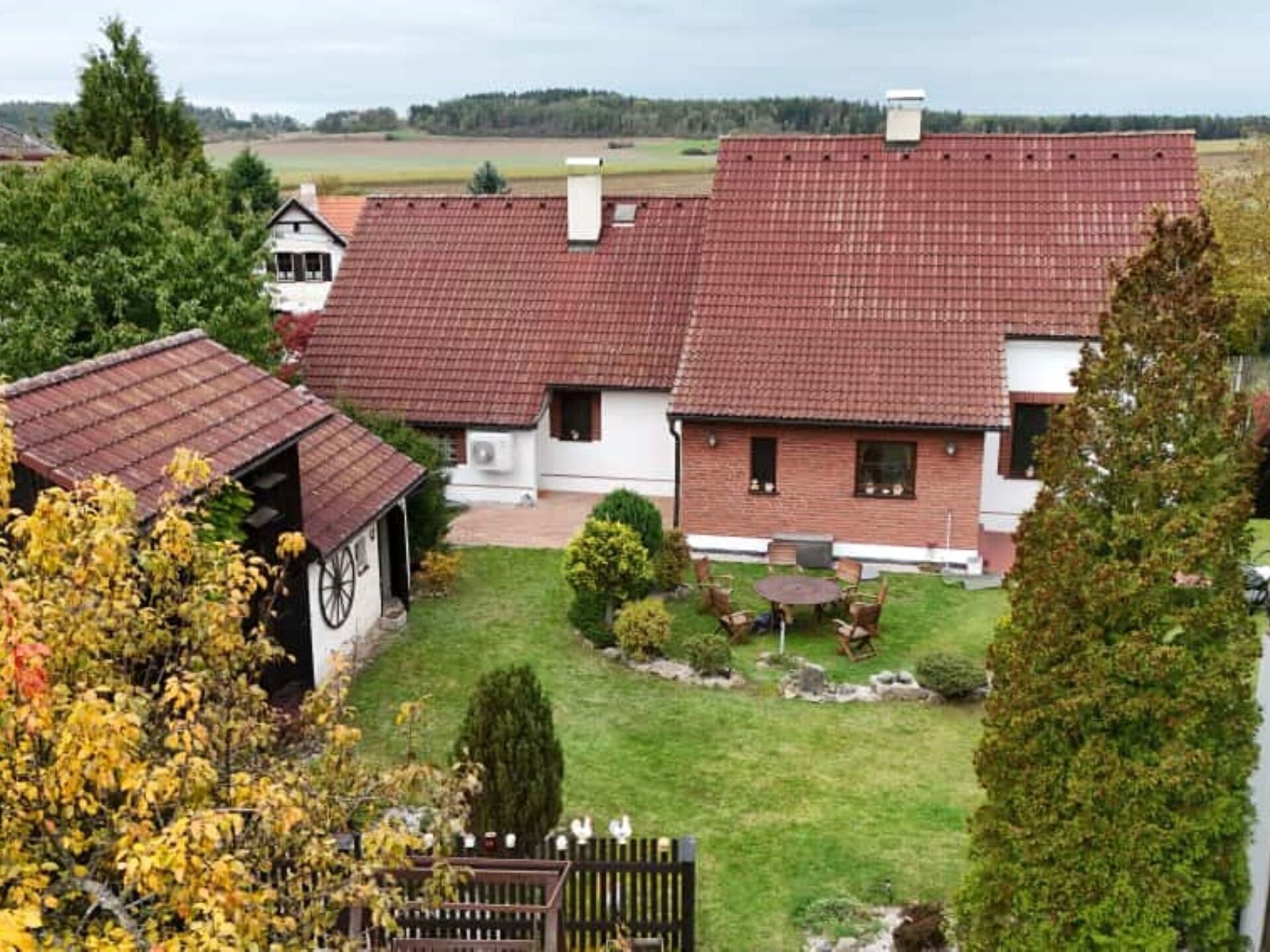 Uma casa de dois andares com telhado de telhas vermelhas, uma pequena garagem anexa e um gramado bem cuidado com área de pátio.