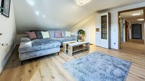 Ein modernes Schlafzimmer im Loft-Stil mit schrägverdeckter Decke, einem großen grauen Sofa, einem Holztisch und einem blauen Teppich.