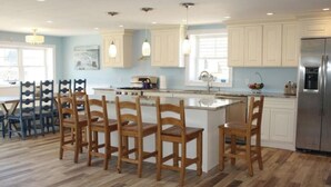 Una cocina amplia con una isla central, sillas de madera y un refrigerador de acero inoxidable.