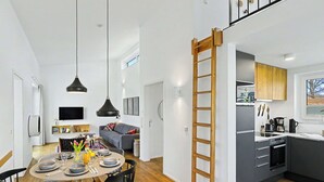 Eine moderne Küche mit grauen Schränken, einer Holzleiter und einer Essecke mit rundem Tisch und Stühlen.