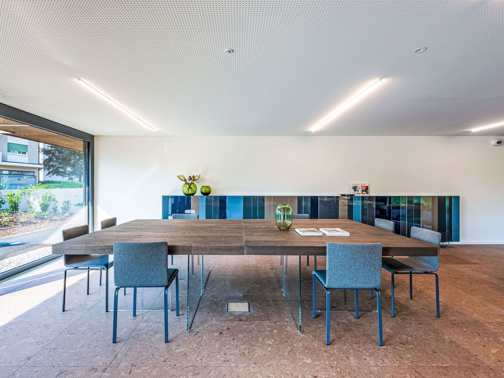 A conference room with a large table, six chairs, and a glass partition.