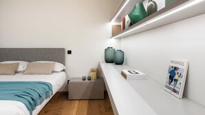 A modern bedroom with a bed, bedside tables, and a shelf with decorative items and a book. - Cosy apartment for 2 people with A/C, WIFI, TV, balcony and panoramic view (Stabio)