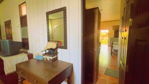 Una habitación con escritorio de madera, televisor, espejo y puerta que da a otra habitación.