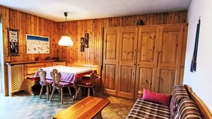 Een gezellige kamer met houten inrichting, een eettafel met stoelen, een bankje en een bank met een geruit plaid.