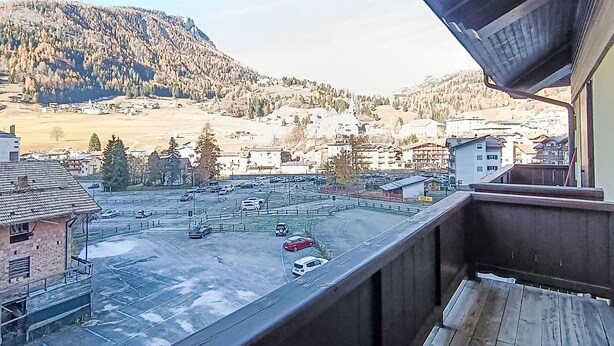 Uitzicht vanaf een balkon over een parkeerplaats en een stad met gebouwen en bergen op de achtergrond.