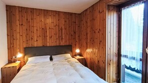 Een slaapkamer met een houten lambrisering, een groot bed met witte beddengoed, twee nachtlampen en een raam met uitzicht.