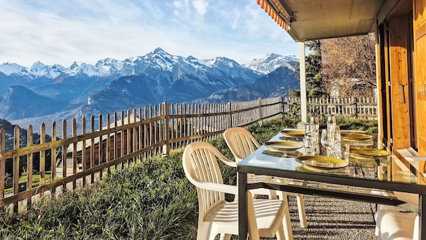 Mesa lista para comer con vista a la montaña, cerca de una valla de madera y un área techada.