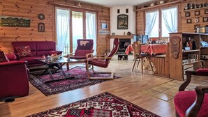 Un interior cálido de cabaña de madera con un sofá rojo, una mesa de comedor con sillas y una chimenea.