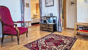 Una sala de estar con un sillón rojo, una mesa de centro de madera, un tapete estampado y una estantería.