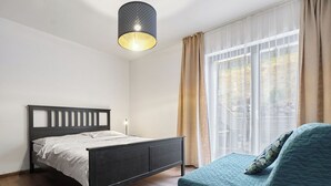 A bedroom with a bed, a bedside table, a lamp, a window with curtains, and a view of the outdoors.