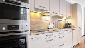 A modern kitchen with stainless steel appliances, a wooden countertop, and light-colored cabinetry.