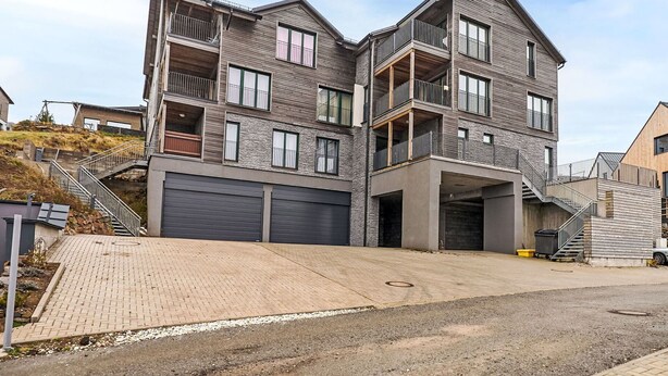 A multi-story residential building with a modern design, featuring balconies, large windows, and a garage.