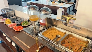 A buffet setup with various food items and a juice dispenser. - VangVieng Avenue Hotel (Vang Vieng)