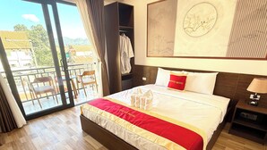 A hotel room with a large bed, a balcony with chairs, and a view of the countryside. - VangVieng Avenue Hotel (Vang Vieng)