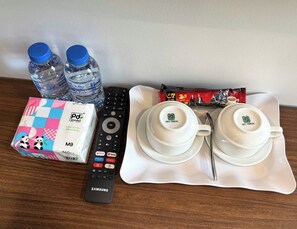 A tray with two white cups, a remote control, a box of tissues, and two water bottles. - VangVieng Avenue Hotel (Vang Vieng)
