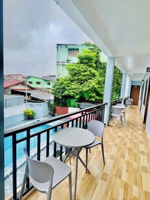 A balcony with a view of buildings and a tree, furnished with chairs and a table. - VangVieng Avenue Hotel (Vang Vieng)