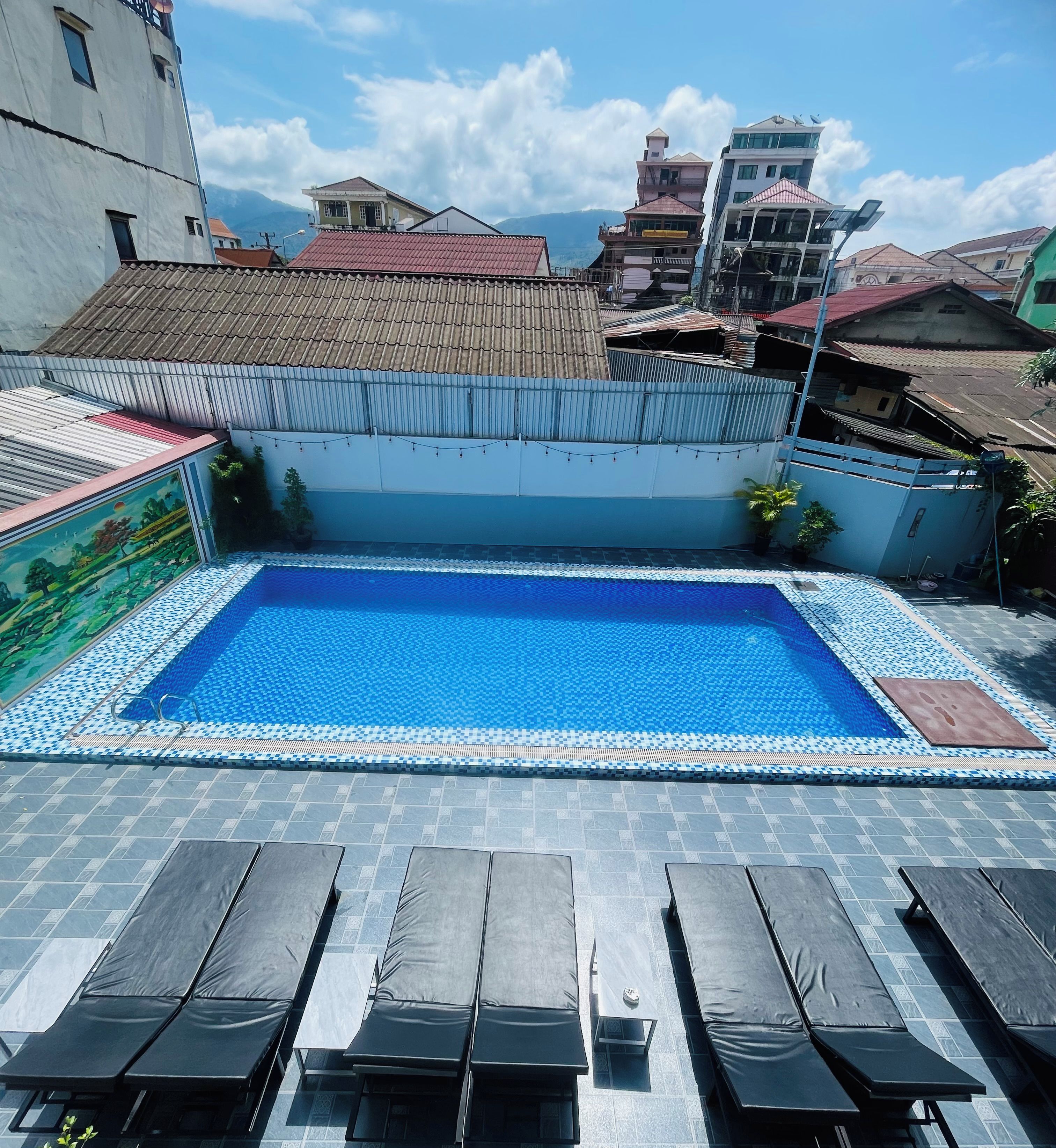 Ein Dachpool mit einer gefliesten Kante, umgeben von Liegestühlen und Blick auf die Stadt.