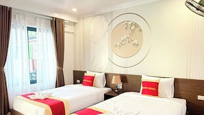 A hotel room with two beds, each with a red and white bedspread, a wooden headboard, and a wall-mounted circular artwork. - VangVieng Avenue Hotel (Vang Vieng)