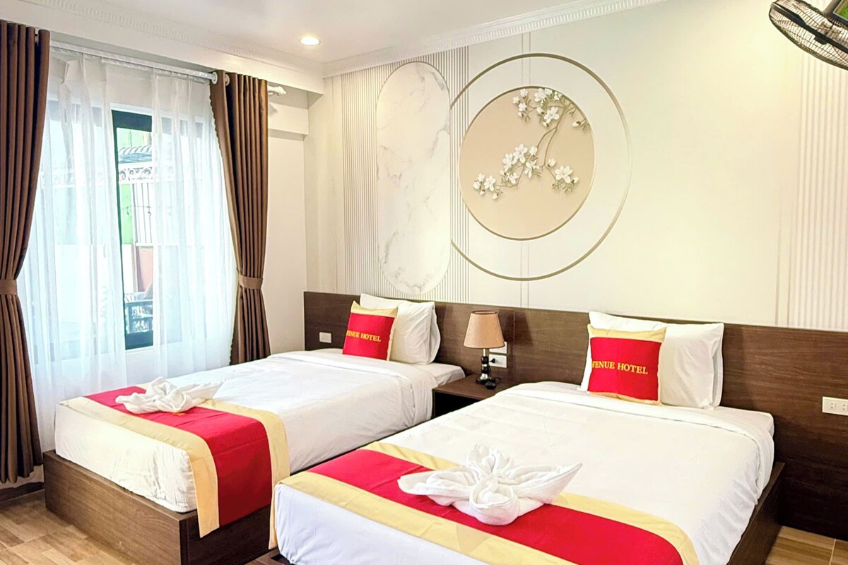 A hotel room with two beds, each with a red and white bedspread, a wooden headboard, and a wall-mounted circular artwork.