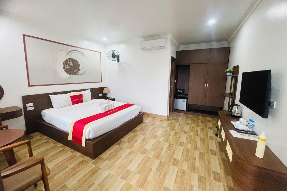 A hotel room with a bed, bedside table, desk, chair, and a TV mounted on the wall.