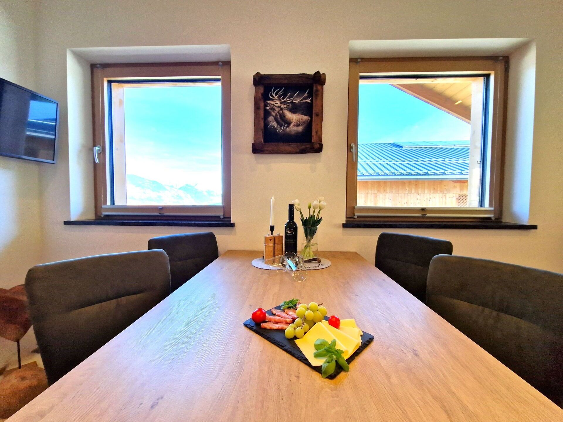 Uma sala de jantar com uma mesa comprida, duas janelas, uma TV montada e um objeto decorativo na parede.