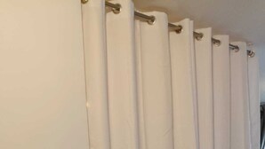Een kamer met een witte gordijn, een houten vloer en een zichtbaar stopcontact.