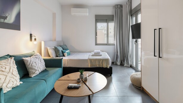 A modern hotel room with a sofa, a bed, a dining table, and a TV. - Cassiopeia - Studio & Balcony in Athens (Athens)