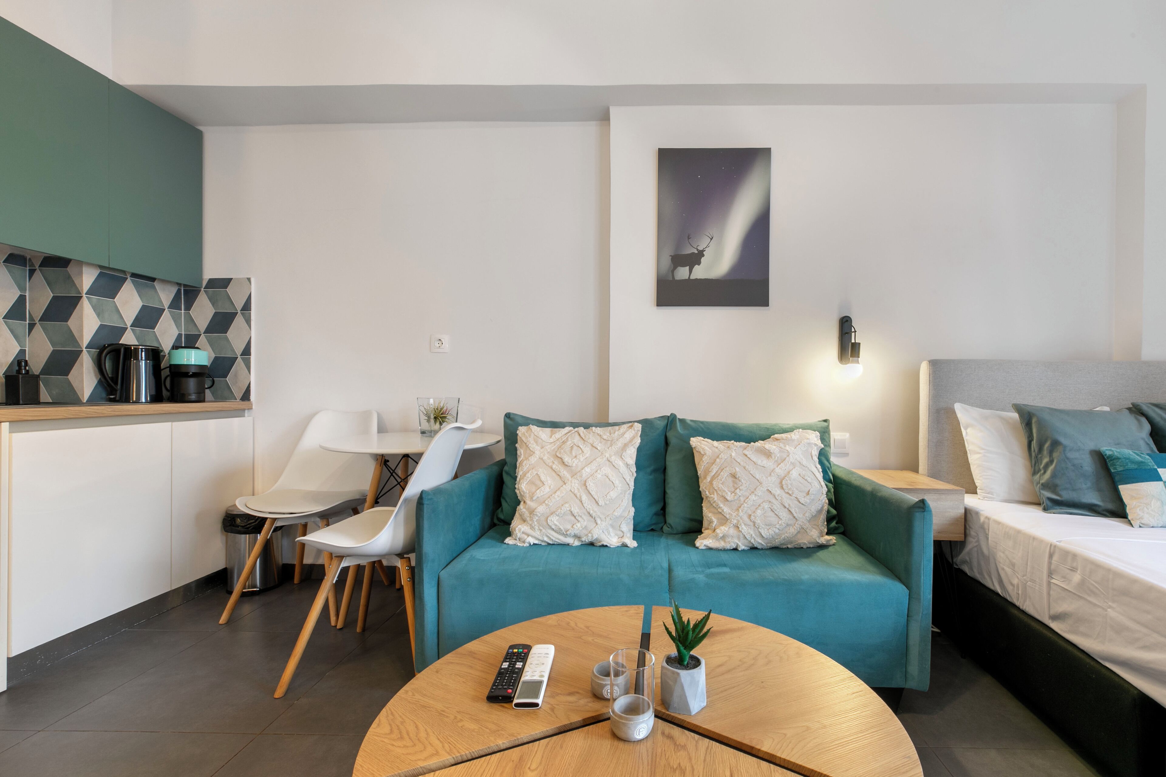 A modern living room with a teal sofa, a round wooden coffee table, a small potted plant, and a painting of a deer on the wall.