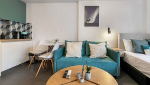 A modern living room with a teal sofa, a round wooden coffee table, a small potted plant, and a painting of a deer on the wall. - Cassiopeia - Studio & Balcony in Athens (Athens)