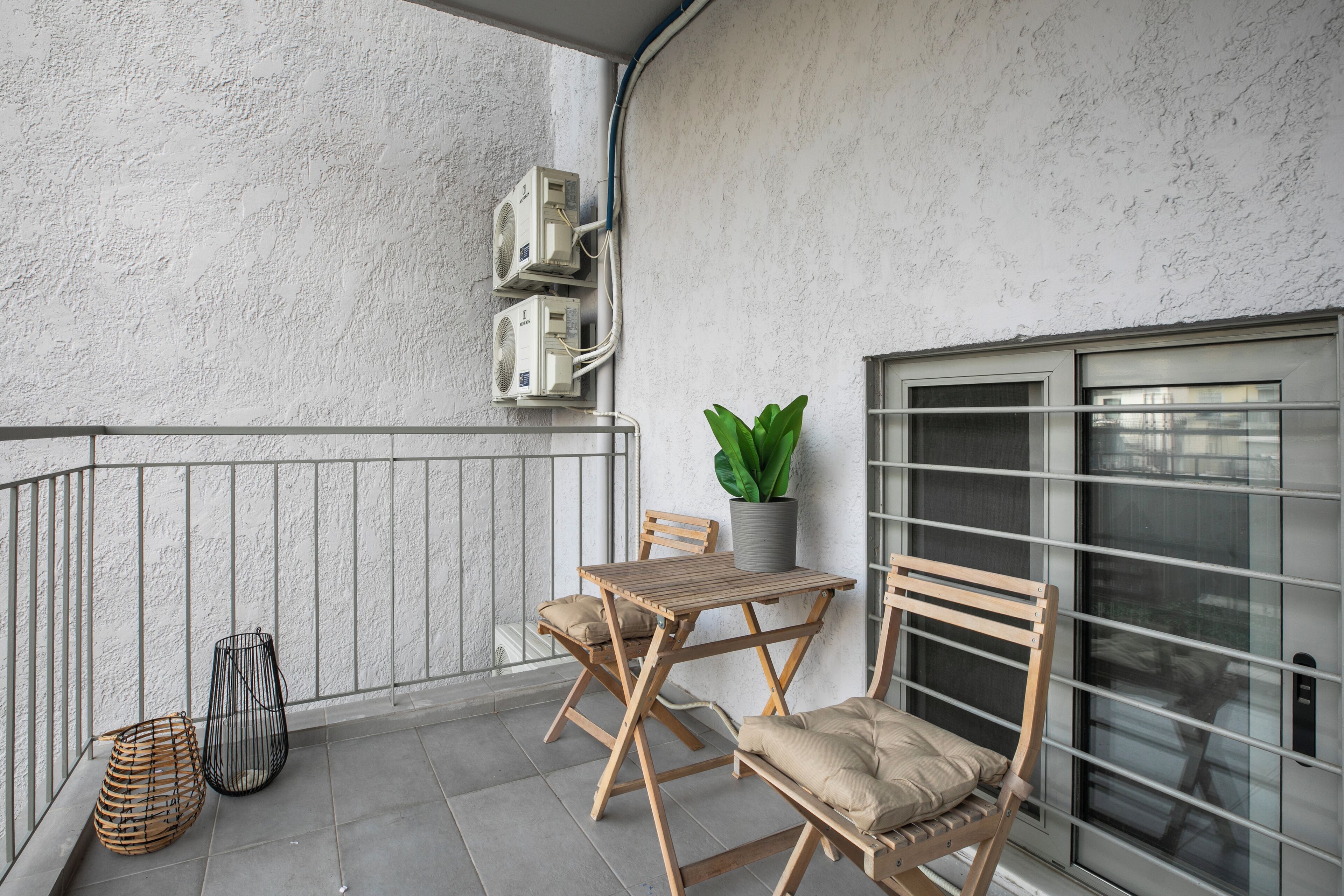 A balcony with a wooden table and chairs, a potted plant, and a metal chair.