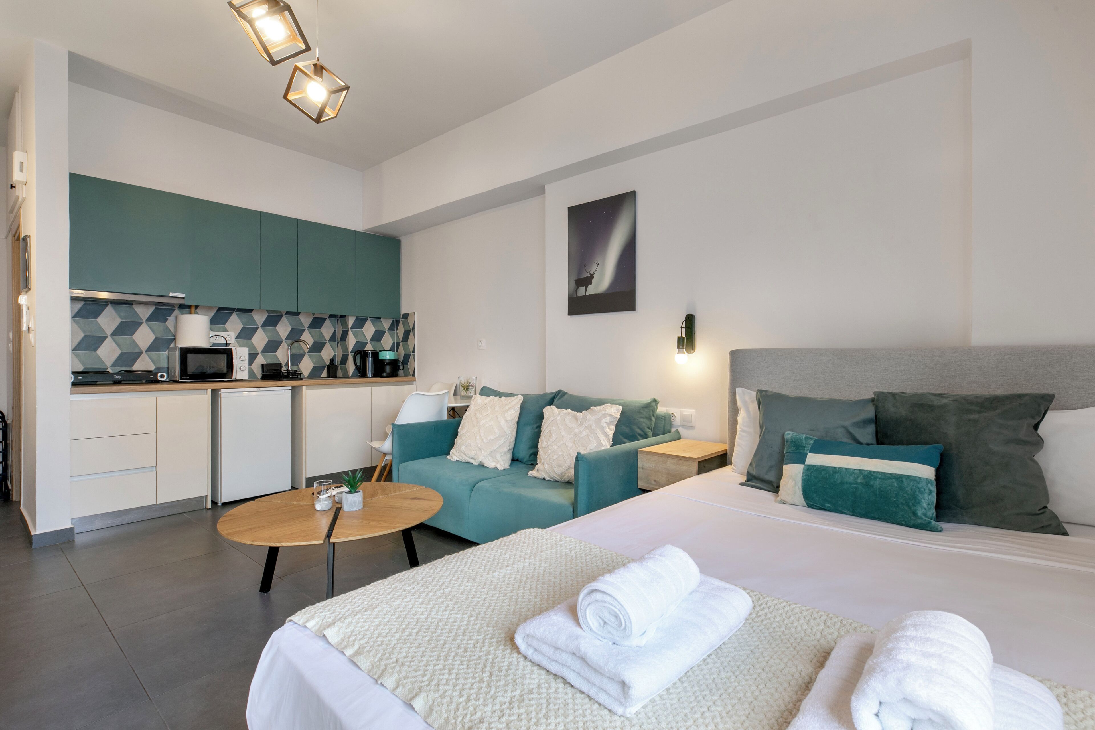 Una habitación de hotel moderna con cama, sofá, pequeña cocina y mesa de comedor.