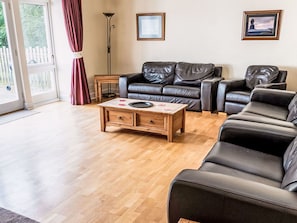 Ein Wohnzimmer mit Couchtisch aus Holz, zwei schwarzen Ledersofas und einer Stehlampe.