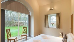 Une chambre avec un grand lit, deux fauteuils, une fenêtre avec des rideaux et une vue sur un jardin.