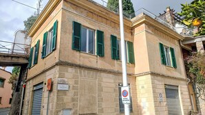Un edificio de dos pisos con contraventanas verdes, una reja metálica y un letrero de no estacionamiento.