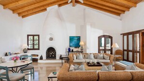 A spacious living room with a high wooden ceiling, a fireplace, a large sofa set, and a dining area with a table and chairs. - Spartilas Villas (Corfu)