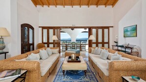 A spacious living room with two wicker sofas, a coffee table, and a view of the mountains through a large window. - Spartilas Villas (Corfu)
