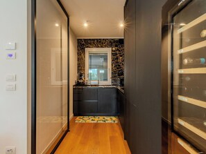 A narrow hallway with a kitchen area featuring a marble backsplash, a refrigerator, and a small countertop with a coffee machine.