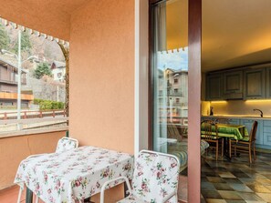 Een balkon met een tafel en stoelen, uitzicht op een woonwijk en een blik op een keuken met blauwe kastjes.