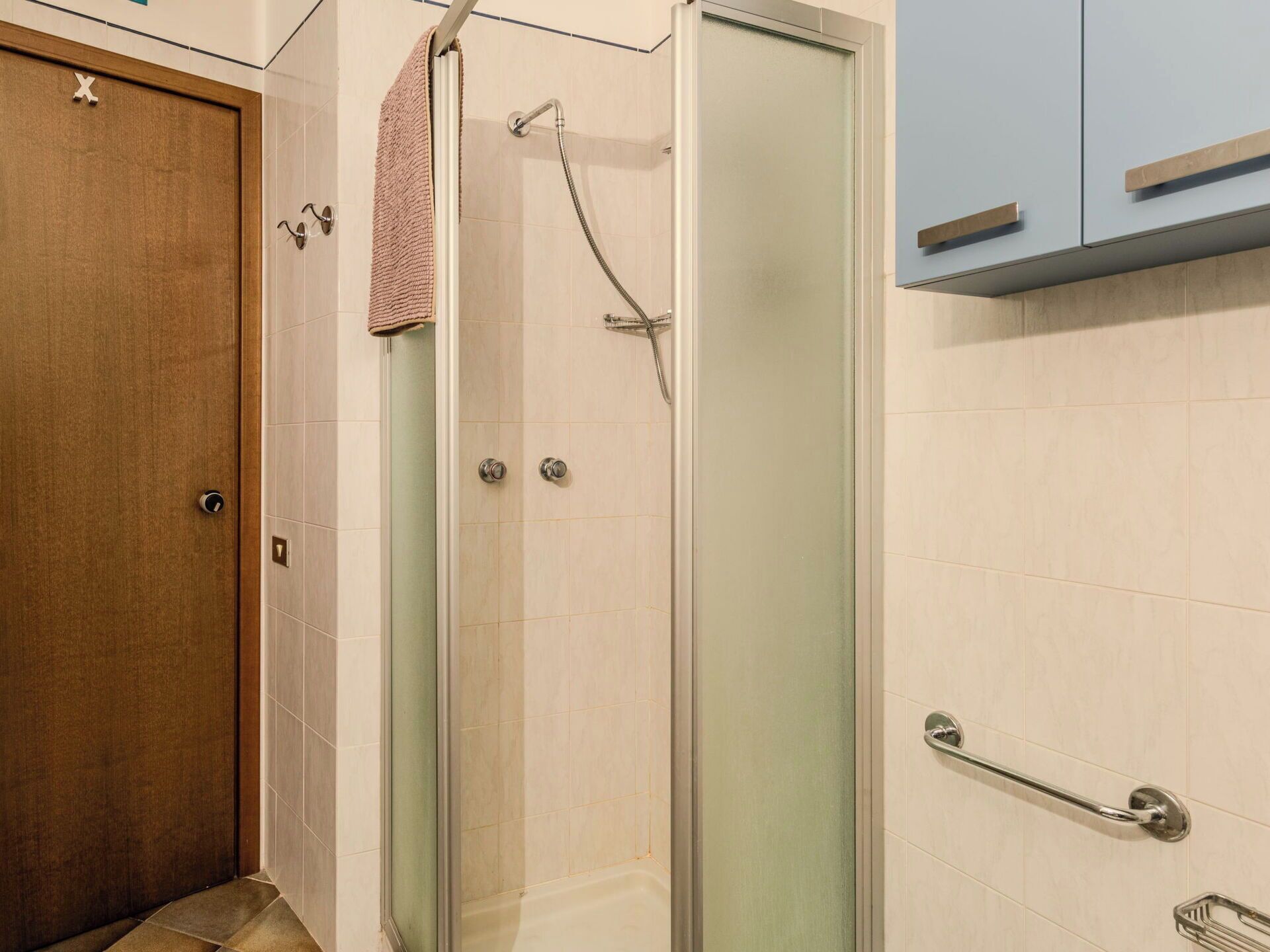 A bathroom with a glass shower enclosure, a wooden door, and a towel hanging on the shower door handle.