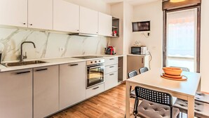 Une cuisine moderne avec un dosseret en marbre, des appareils en acier inoxydable et un coin repas comprenant une table et des chaises.