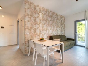 Une cuisine moderne avec une table et des chaises blanches, un panier de fruits et un canapé vert.