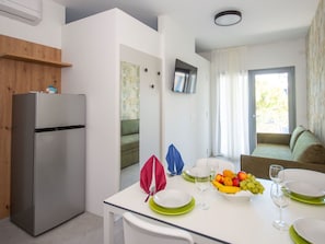 A modern kitchen with a refrigerator, dining table set with plates, glasses, and fruit. - Cosy apartment for 4 people with WIFI, A/C, TV, terrace and pets allowed (San Michele Al Tagliamento)