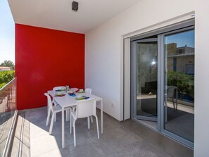 Ein Balkon mit einem weißen Tisch, gedeckt für zwei Personen, einer roten Wand und einer Glastür zum Garten.
