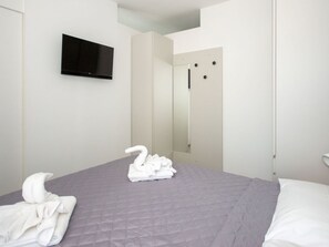 Ein Hotelzimmer mit einem Bett, einem an der Wand befestigten Fernseher und einem Spiegel an der Tür.