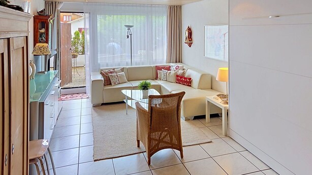 A modern living room with a sofa, a dining table, and a wicker chair. - Lovely apartment for 4 guests with WIFI, TV, balcony, pets allowed and panoramic view (Laax)