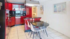 A compact kitchen with red cabinets, a black countertop, and a glass dining table with four chairs. - Lovely apartment for 4 guests with WIFI, TV, balcony, pets allowed and panoramic view (Laax)