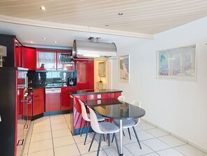 A compact kitchen with red cabinets, a black countertop, and a glass dining table with four chairs.