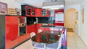 A modern kitchen with red cabinetry, a glass dining table, and a stainless steel range hood. - Lovely apartment for 4 guests with WIFI, TV, balcony, pets allowed and panoramic view (Laax)